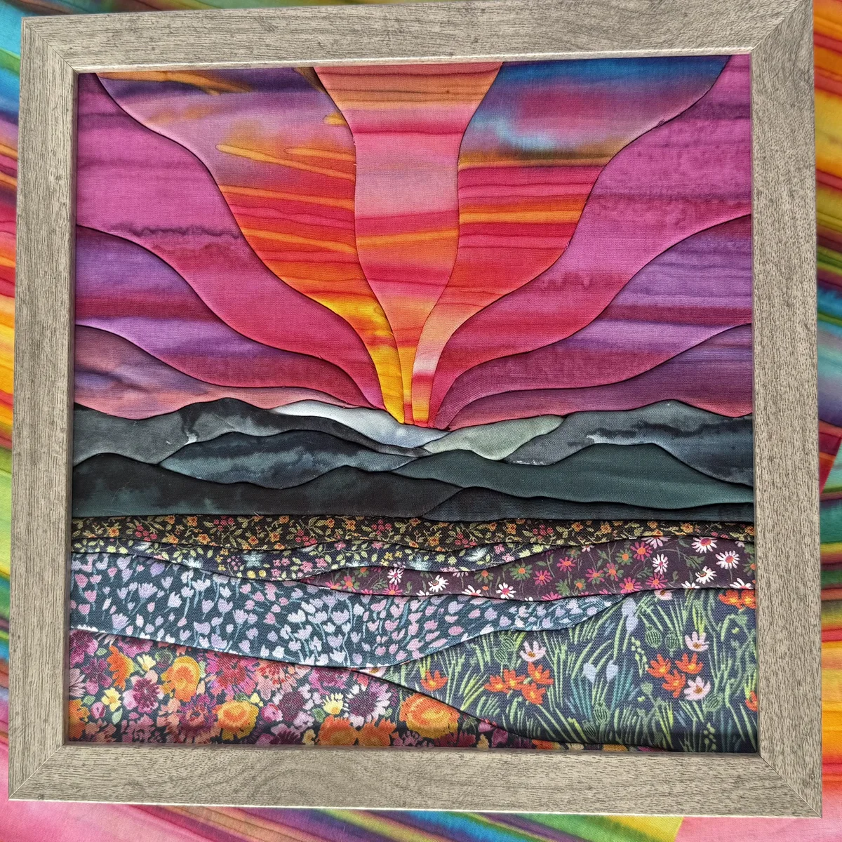 A kinusaiga fabric landscape of a sunrise over the Cascade mountains with a wildflower meadow, made entirely from quilting cotton tucked into a carved foam board